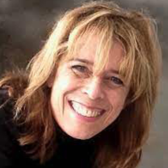 Veronique Mackenzie: A middle-aged blonde woman with long hair and straight across bangs. SHe is wearing a black turtle neck and smiling into the camera.